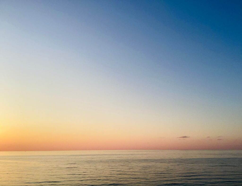 A serene sunset over a calm ocean, with vibrant pastel colors in the sky.